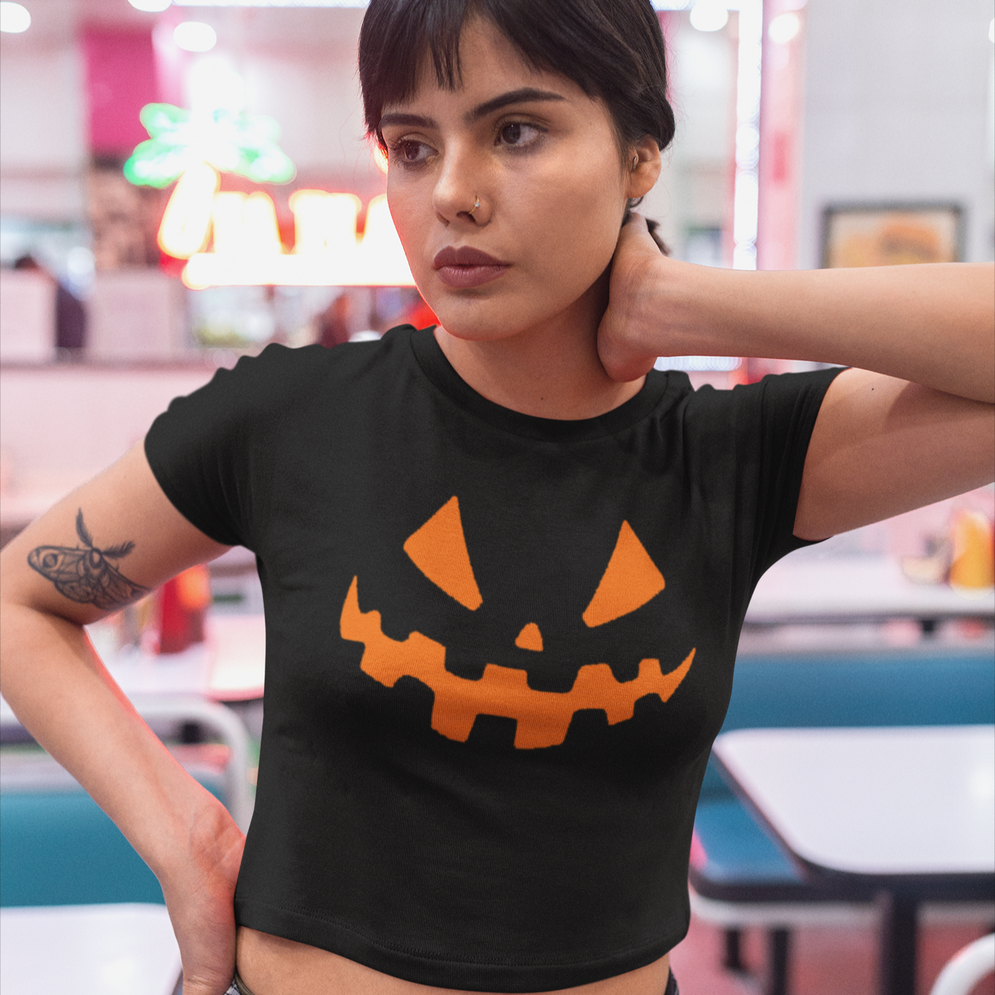 Person wearing a black t-shirt with an orange jack-o'-lantern face design in a casual setting.